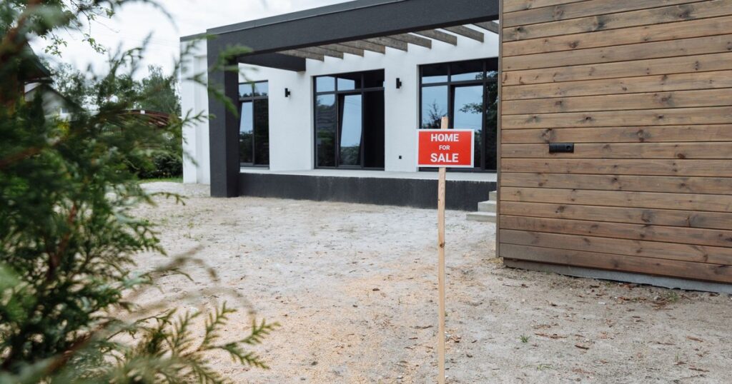 Home for sale sign posted in front of a modern house