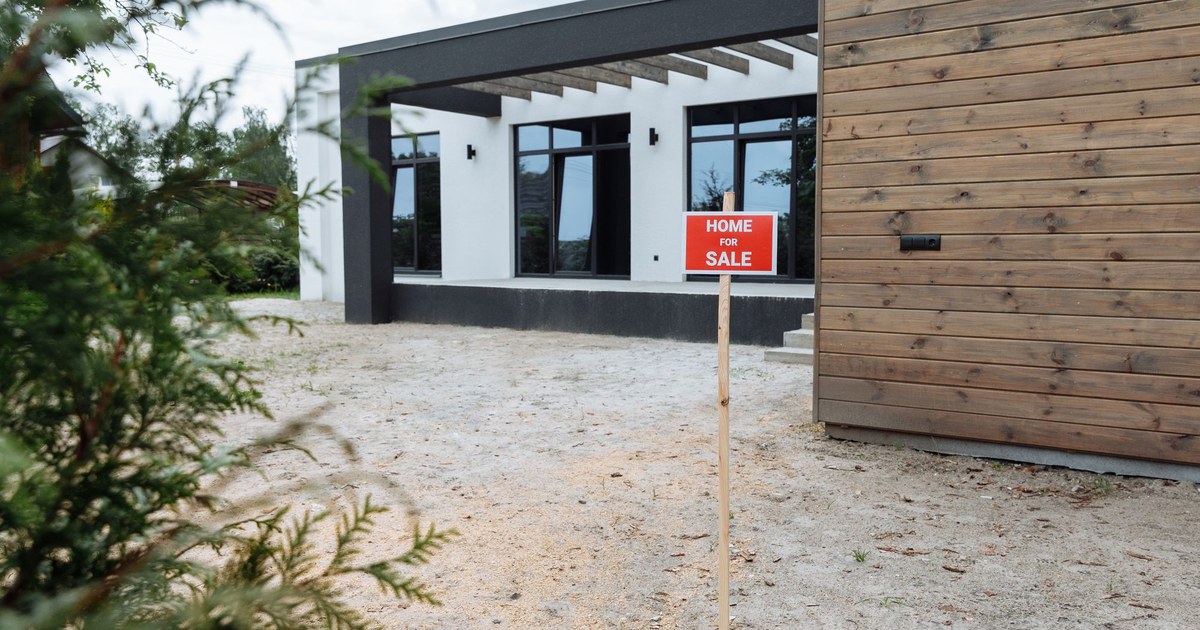 Home for sale sign posted in front of a modern house