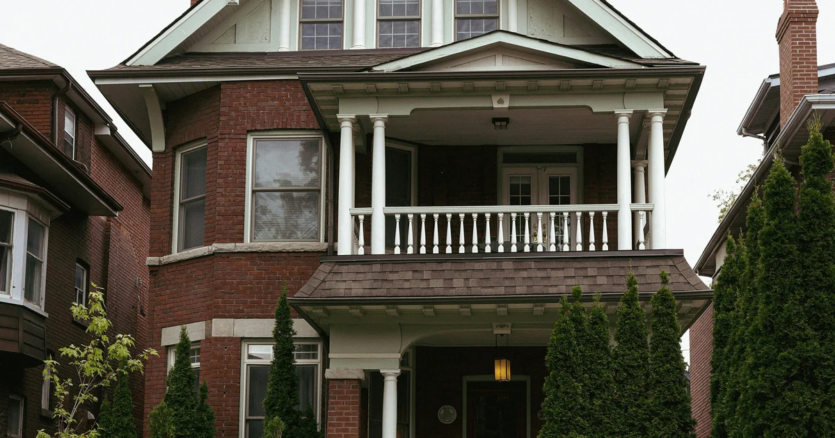 Red brick semi-detached homes with front porches on a tree-lined street in Danforth Village, East Toronto