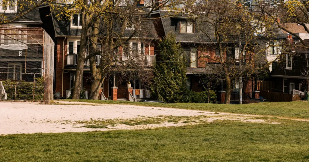 Red brick semi-detached row houses with balconies on a tree-lined street in Greenwood-Coxwell, Toronto