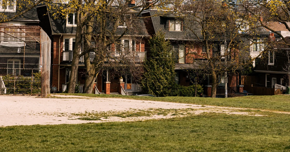 Row of brick semi-detached homes on a tree-lined street in Greenwood-Coxwell, Toronto