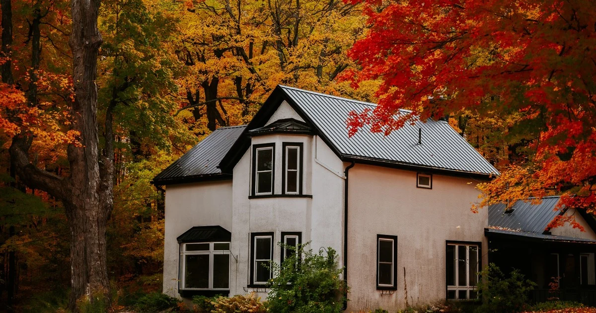 A white century home with a dark metal roof surrounded by red and gold autumn trees in Ontario